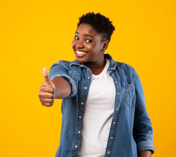 Cheerful Overweight African American Lady Gesturing Thumbs Up To Camera Approving Something Posing Standing On Yellow Studio Background. I Like It, Thumbs-Up Gesture Concept